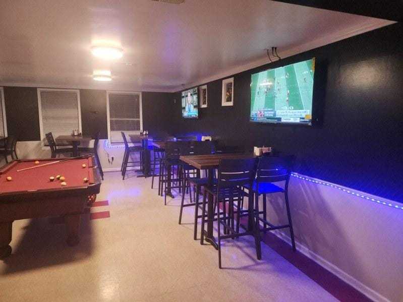 Pool table and TVs in a lounge with high tables and blue lighting.